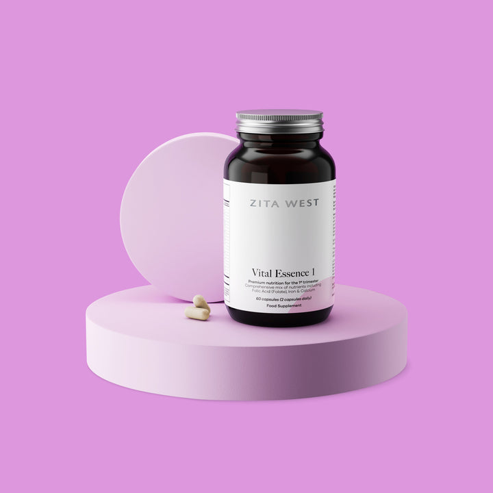 Bottle of Zita West Vital Essence 1 supplement on a pink display with two capsules beside it