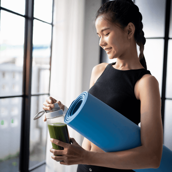 Woman holding a rolled yoga mat and a bottle of green smoothie