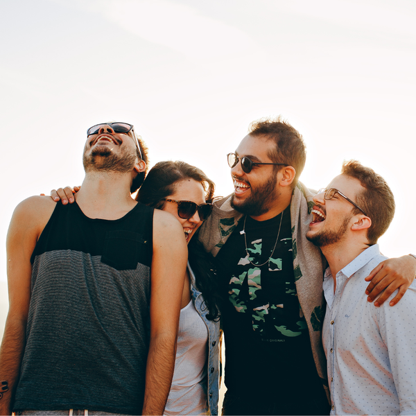 Four friends laughing together outdoors wearing sunglasses