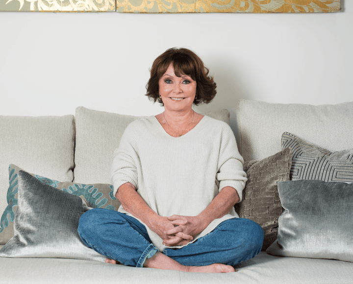 Smiling woman sitting cross-legged on a sofa with patterned cushions