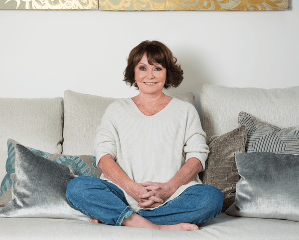 Smiling woman sitting cross-legged on a sofa with patterned cushions