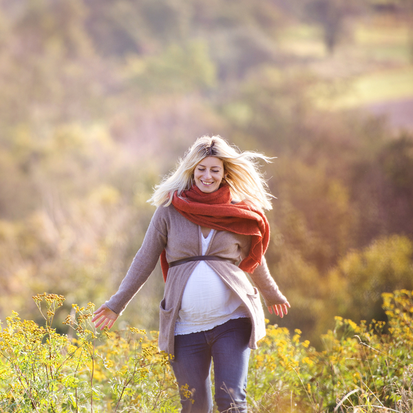 Pregnant woman smiling as she walks through a golden autumn field wearing a red scarf