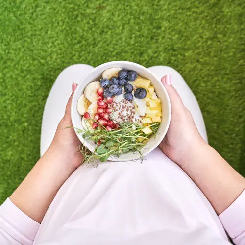 Overhead view of a pregnant woman holding a bowl of fruit and yogurt topped with blueberries, banana and pomegranate seeds