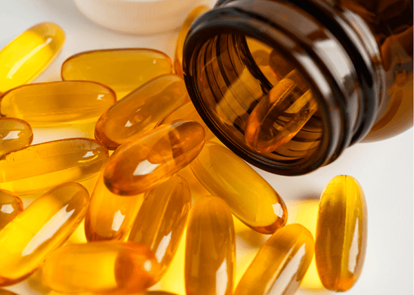 Golden omega-3 softgel capsules spilling out of a dark amber bottle