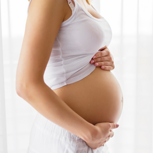 Close-up of a pregnant woman's belly in a white tank top with her hand resting on it