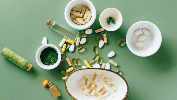 Assorted vitamin capsules and powders in bowls and jars on a green background