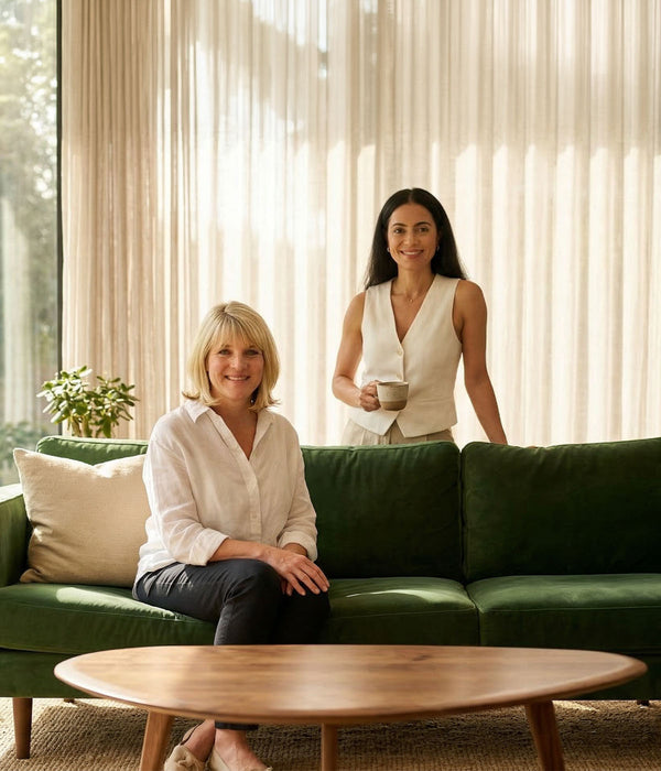 Two women in a living room, one seated on a green sofa and one standing holding a cup