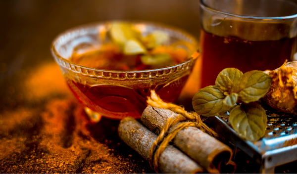 Cinnamon sticks, mint leaves and ginger beside a glass cup of spiced tea