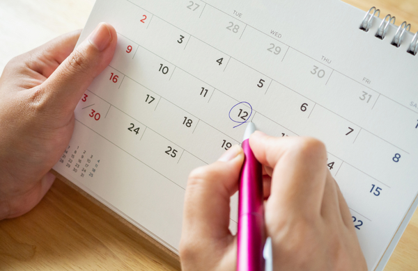 Hand circling a date on a calendar with a pen