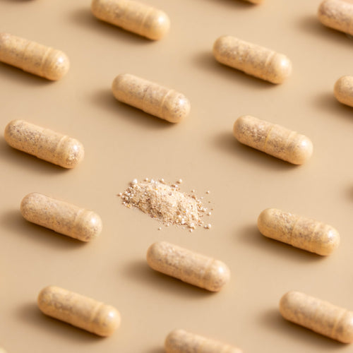 Rows of tan supplement capsules with a small pile of powder in the centre