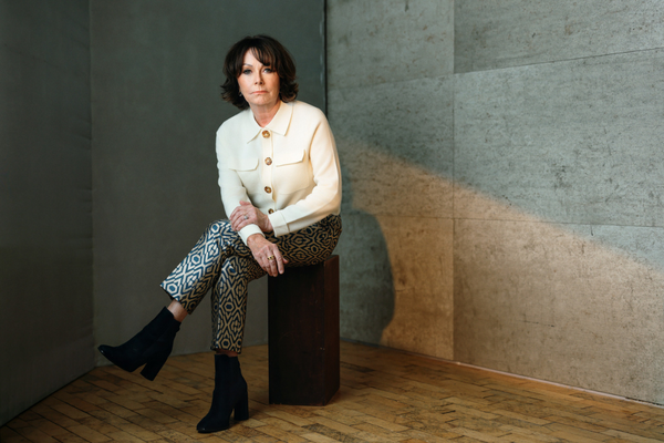 Woman in a white jacket sitting on a wooden block against a concrete wall