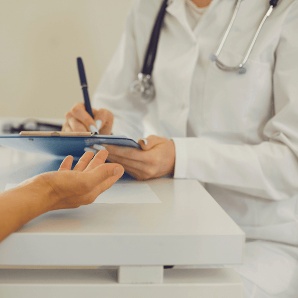 Doctor writing on a clipboard while a patient's hand reaches toward the table