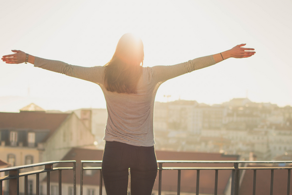 Woman with arms outstretched on a balcony overlooking a sunlit cityscape