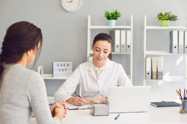 Doctor writing on a clipboard while talking with a patient in an office