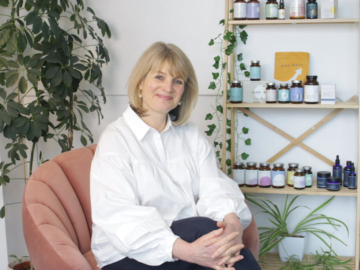 Fertility nutritionist Isabelle Obert seated in a pink chair beside a shelf of Zita West supplements