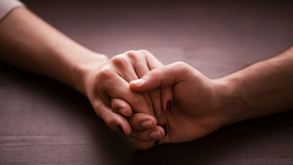 Two hands clasped together in comfort on a wooden table