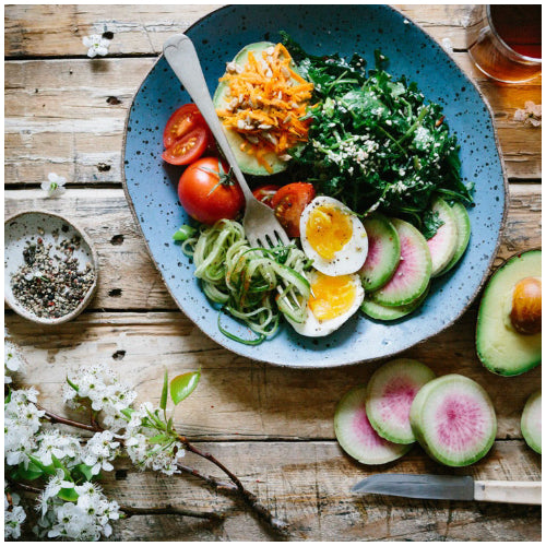 Overhead view of a healthy bowl with avocado, boiled egg, tomatoes, kale and courgette noodles