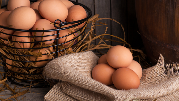 Wire basket of brown eggs surrounded by straw beside eggs wrapped in burlap