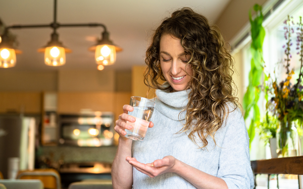 Woman smiling while holding a supplement capsule and a glass of water