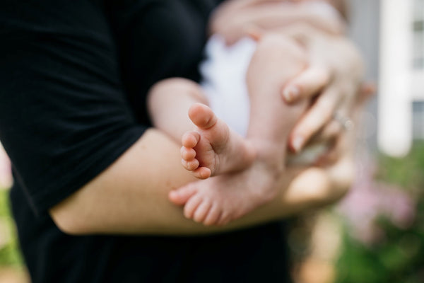 Close-up of a newborn baby's bare feet held gently in an adult's hands outdoors