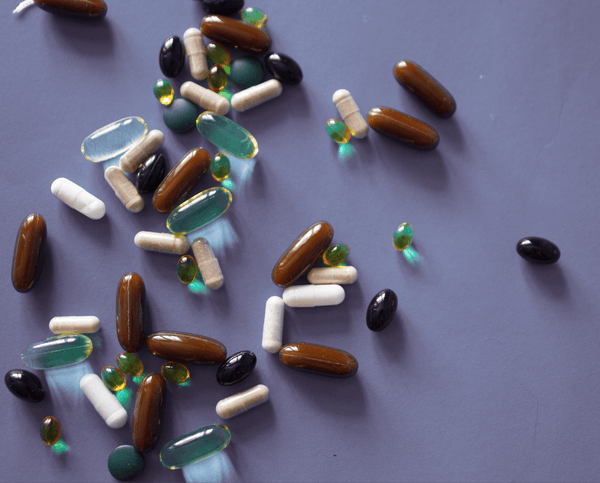 Assorted colorful supplement capsules scattered on a grey-purple surface