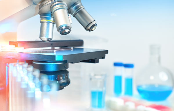 Microscope lens close-up beside laboratory test tubes filled with blue liquid