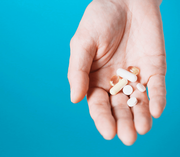 Hand holding an assortment of white and gold supplement capsules against a blue background