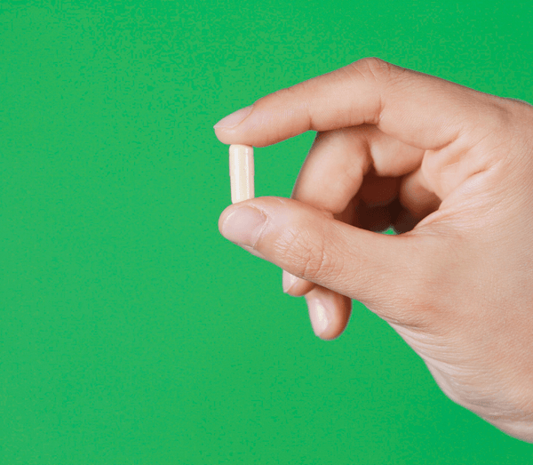 Hand holding a single beige capsule against a green background