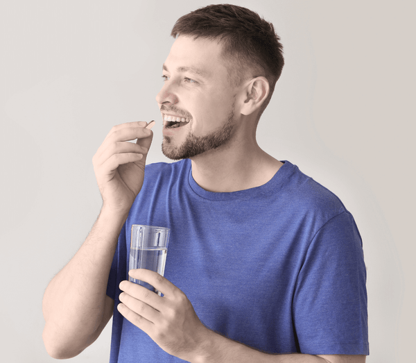Man taking a capsule with a glass of water in hand