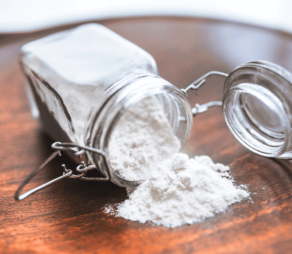 White powder spilling out of a glass jar onto a wooden surface