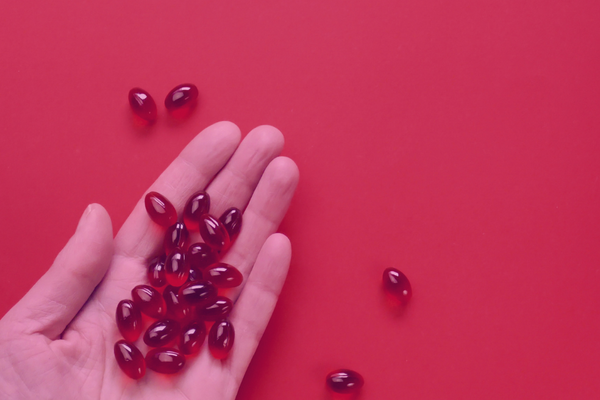 Hand holding reddish softgel capsules against a red background