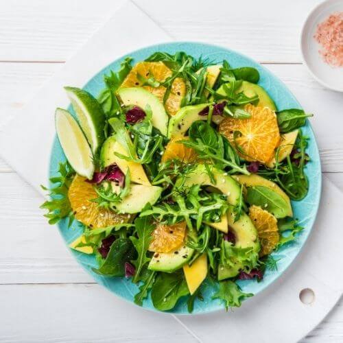 Overhead view of a green salad with avocado, orange segments and mixed leaves on a blue plate