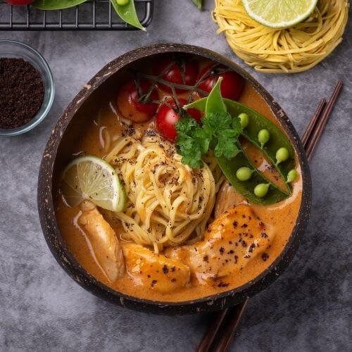 Bowl of Thai-style coconut curry noodle soup with chicken, cherry tomatoes and snow peas