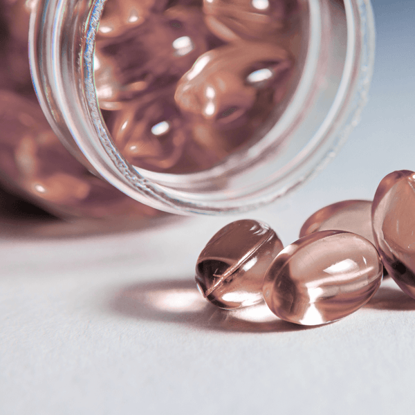 Pink softgel capsules spilling out of an open jar