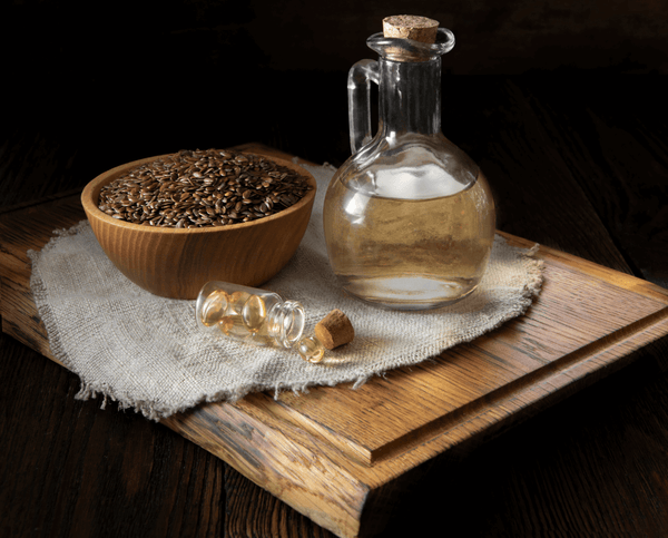 Bowl of flax seeds beside glass bottles of oil on a wooden board