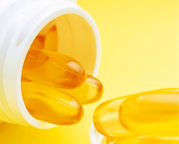 Golden omega-3 softgel capsules spilling out of a white bottle