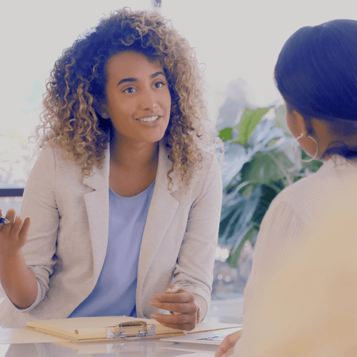 Two women having a discussion at a table with a notebook and pen