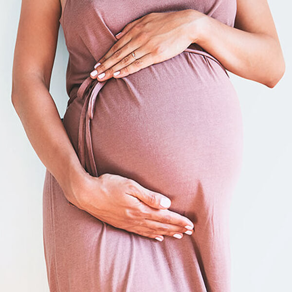 Close-up of a pregnant woman in a pink dress cradling her belly with both hands