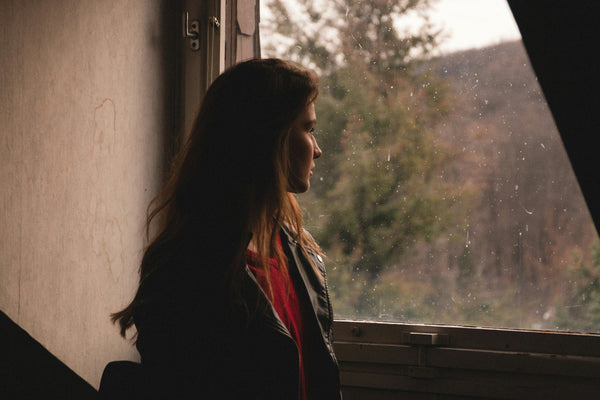 Woman in profile looking out a rain-speckled window at trees