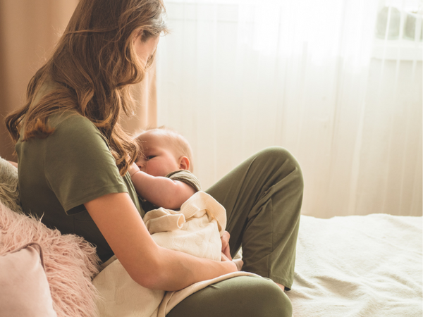 Mother sitting by a window breastfeeding her baby at home