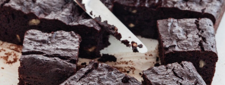 Stacked squares of chocolate brownie on a wooden board with a serving knife