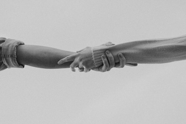 Black and white close-up of two people holding hands, arms outstretched