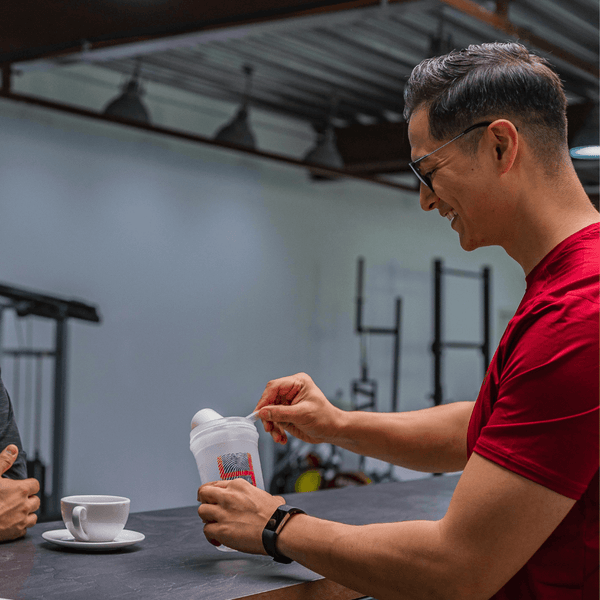 Man in a gym pouring supplement powder into a shaker bottle