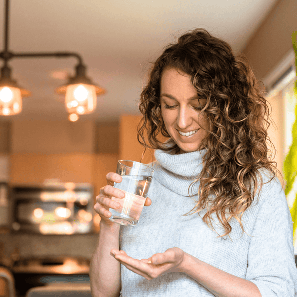 Woman holding a glass of water and a supplement capsule in her hand