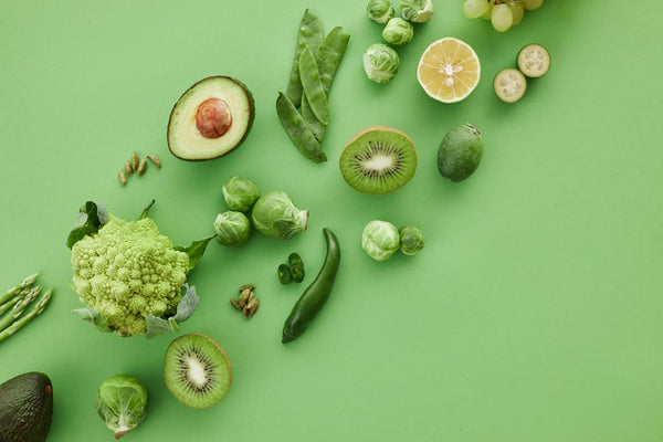 Overhead flat-lay of green vegetables and fruits including avocado, kiwi and brussels sprouts