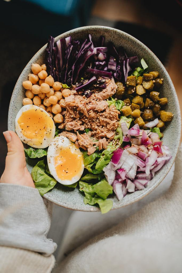 Hand holding a bowl of tuna salad with soft-boiled eggs, chickpeas and red cabbage