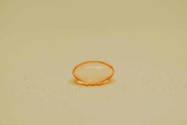 Single orange vitamin E softgel capsule on a light textured surface