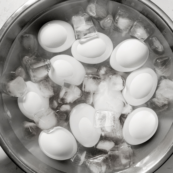 Eggs surrounded by ice cubes in a metal bowl