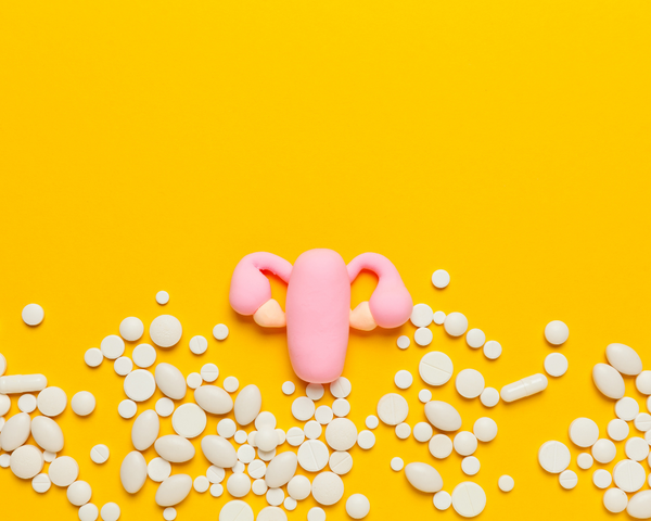 Illustration of a pink uterus surrounded by scattered white pills on a yellow background