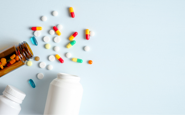 Assorted pills and capsules spilled from bottles on a light blue surface